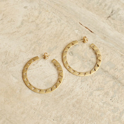 Gold hoop earrings with geometric design on a beige stone surface